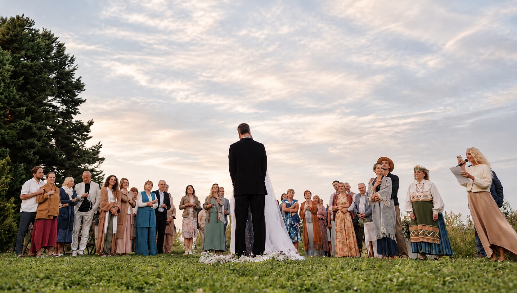 A couple sharing an intimate outdoor ceremonial moment surrounded by their guests